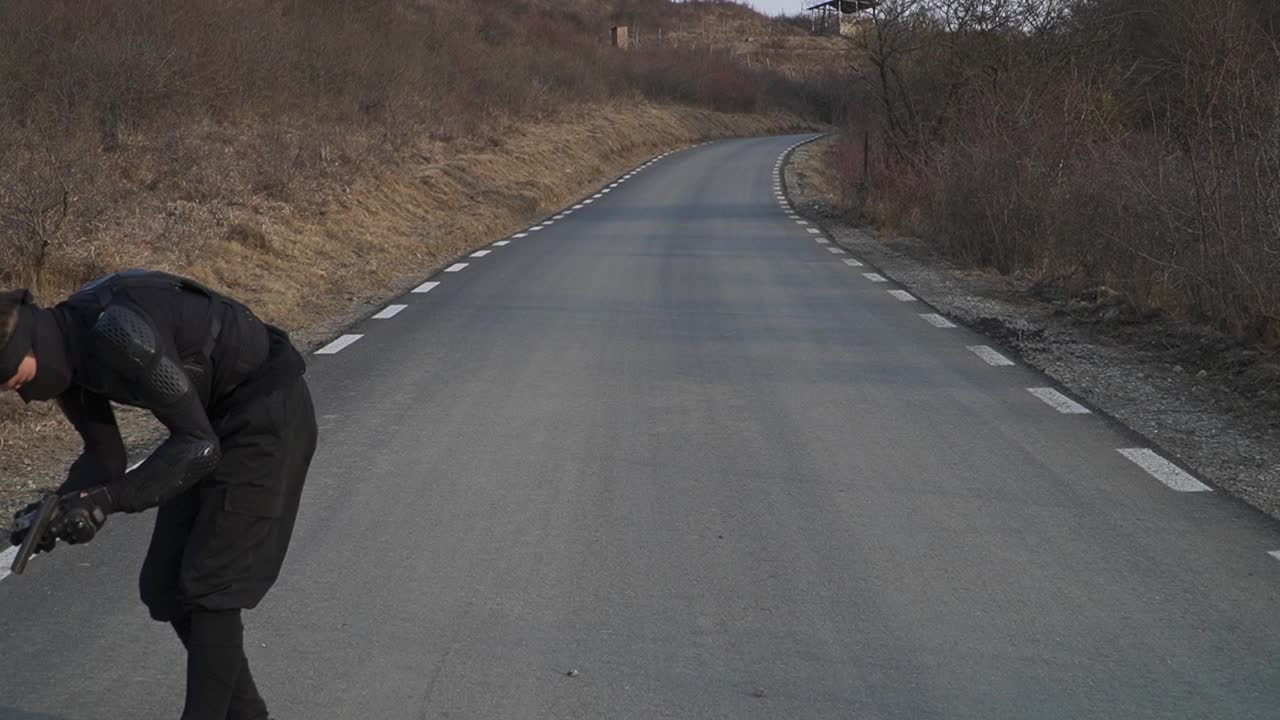 A masked ninja in black tactical gear assumes a combat stance on an empty road, ready for action. His intense focus and controlled posture evoke stealth, discipline, and martial arts mastery