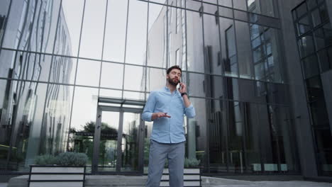 Hombre-Atractivo-Hablando-Por-Teléfono-En-Un-Moderno-Edificio-De-Cristal.-Gerente-Trabajando-Afuera