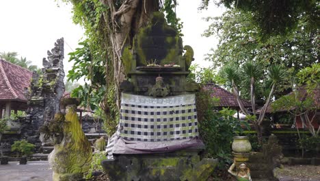 Balinese-Masceti-Temple,-Religious-Statues,-Incense,-Flowers-and-Praying-Elements-for-the-Hindu-Gods-of-Bali,-Indonesia,-Gianyar-Regency,-Worshiping-Atmosphere,-Moss-on-Stone,-60-Fps