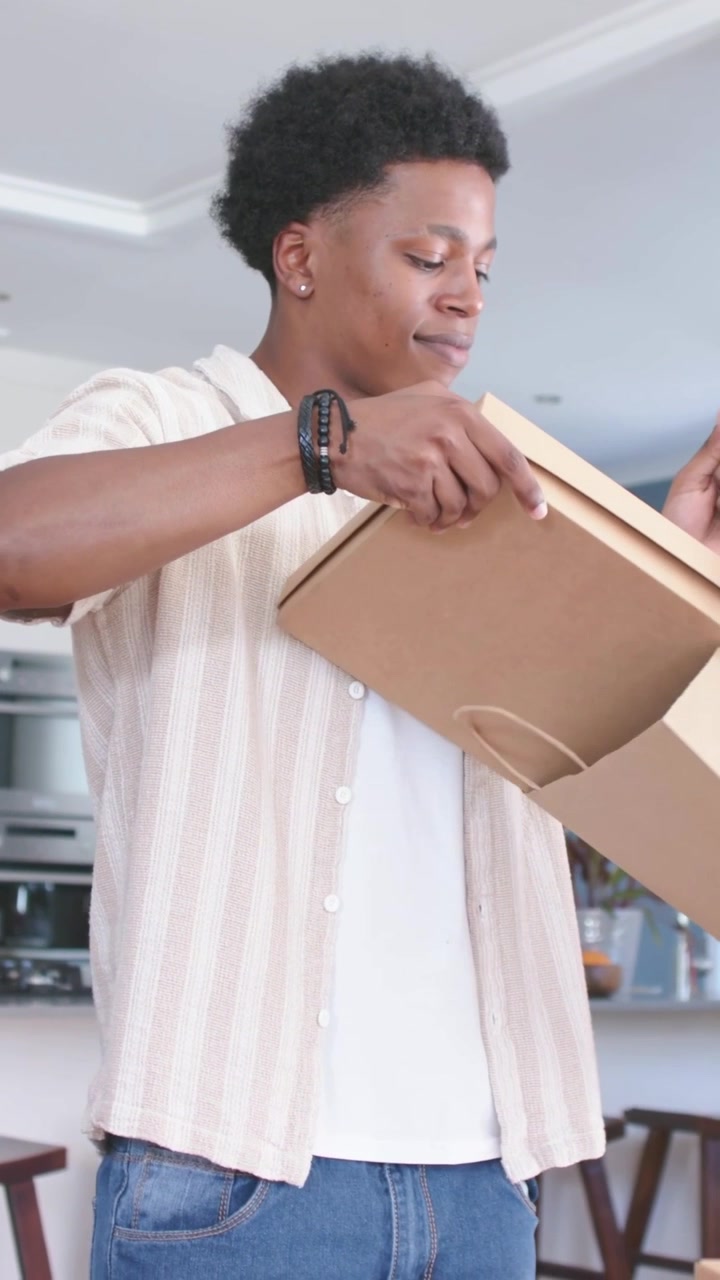African American man after shopping lifting and unpacking paper bag at counter, checking flat boxes