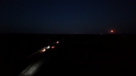 traffic on american highway at night with full moon. aerial wide shot. headlights of cars on street. dark blue colored sky after blue hour in usa