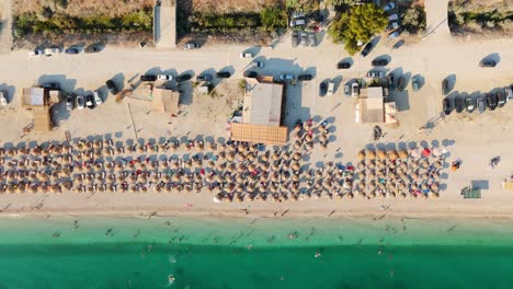 a beachside area with cars, buildings, and umbrellas under the summer sun, aerial view