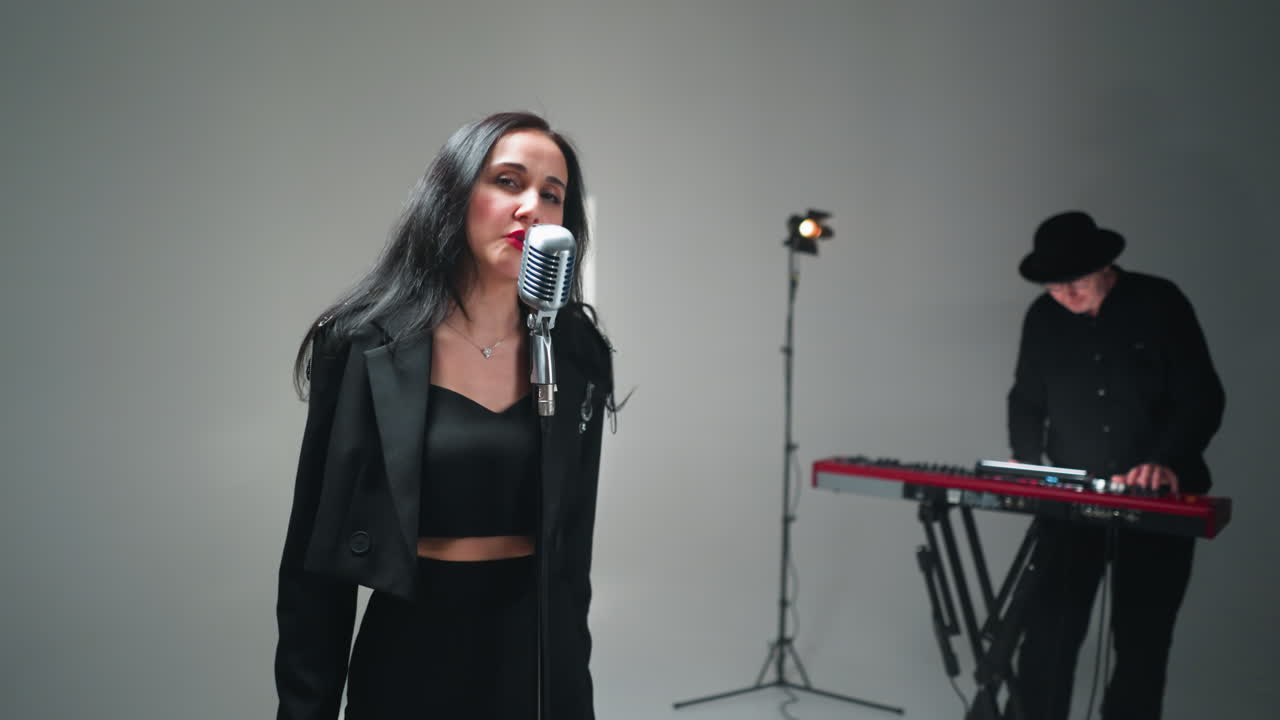 vocalista femenina en negro actuando en un micrófono vintage en un entorno de estudio minimalista, usando gestos de mano expresivos