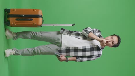 full body of asian male traveler with luggage and passport looking at camera and making shh gesture while standing in the green screen background studio