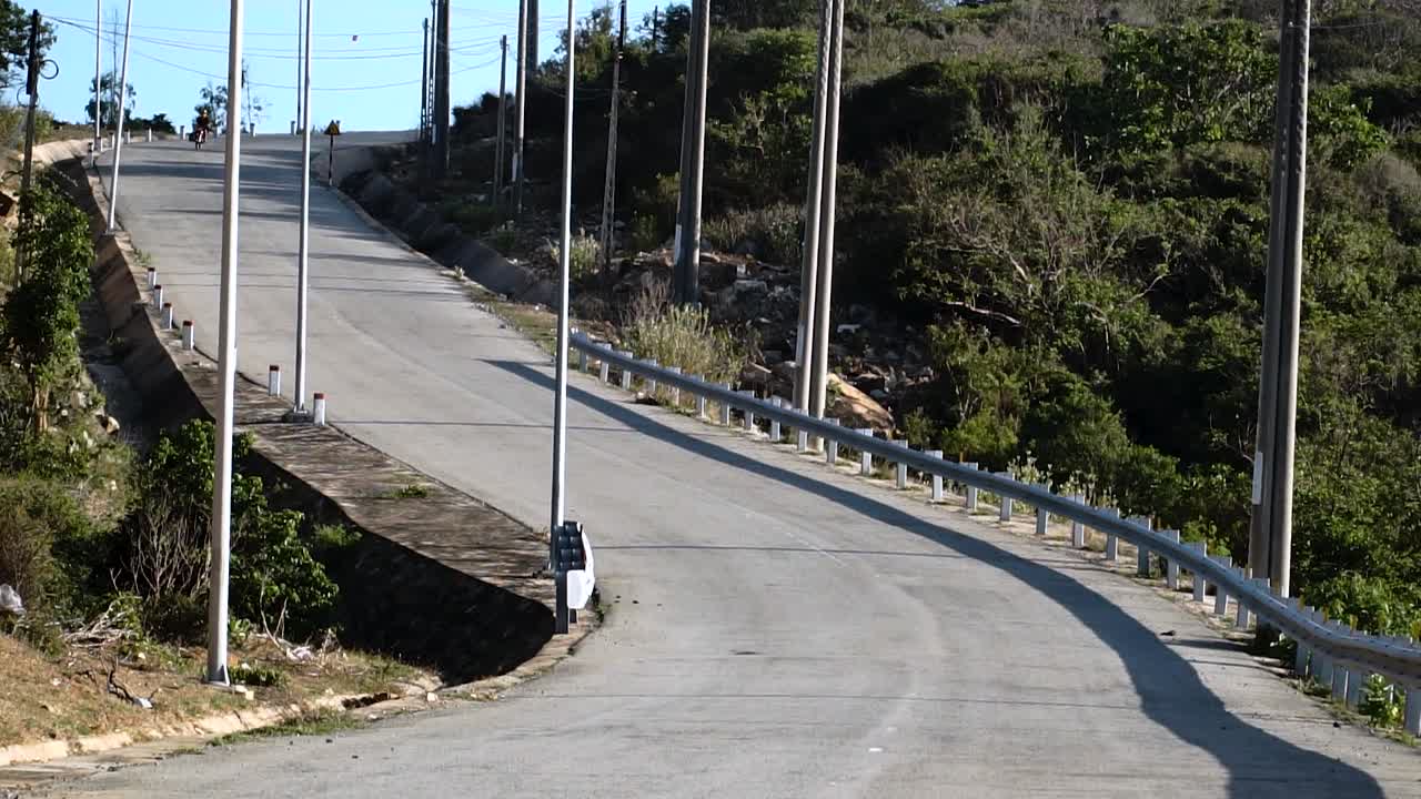 화창한 날 베트남 닌 투언에 있는 빈 하이 근처 거리에서 검은 카이트보드를 들고 있는 노란색 헬멧을 쓴 오토바이 운전자