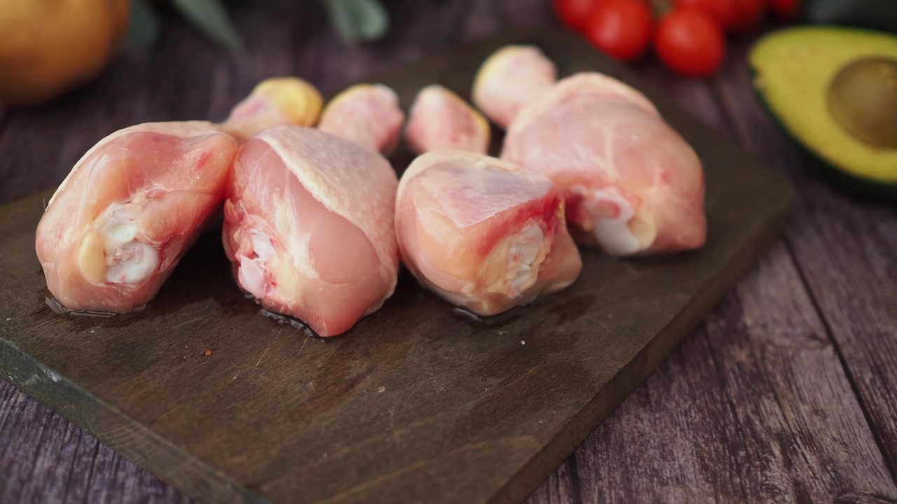 Fusi di pollo crudi disposti su un tagliere di legno