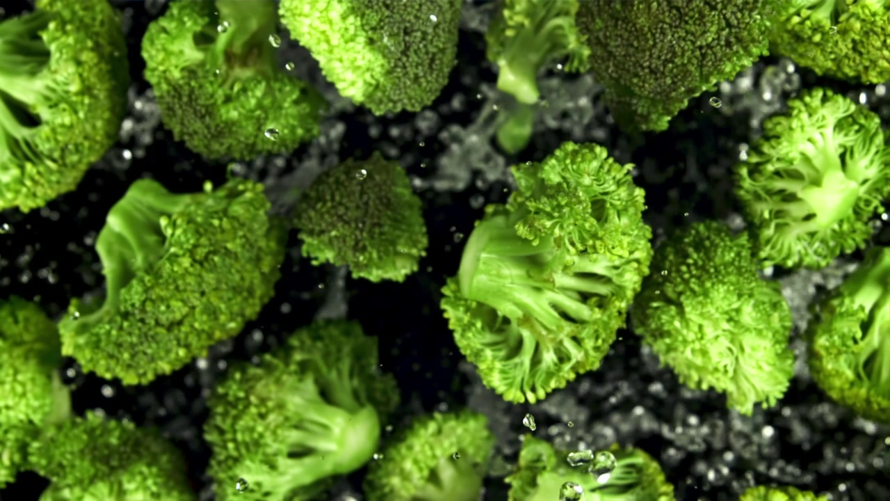 Cimette di broccolo verde fresco che schizzano con l'acqua in super slow motion