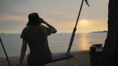 mujeres disfrutando de la vista del atardecer en la playa mientras están sentadas en un columpio de cuerda