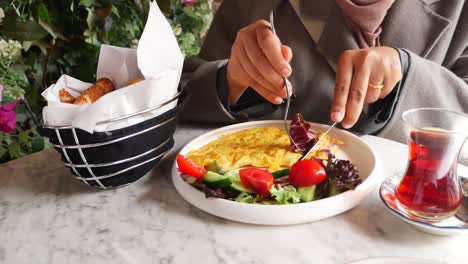 mujer disfrutando de un delicioso desayuno de tortilla, ensalada y té en un café