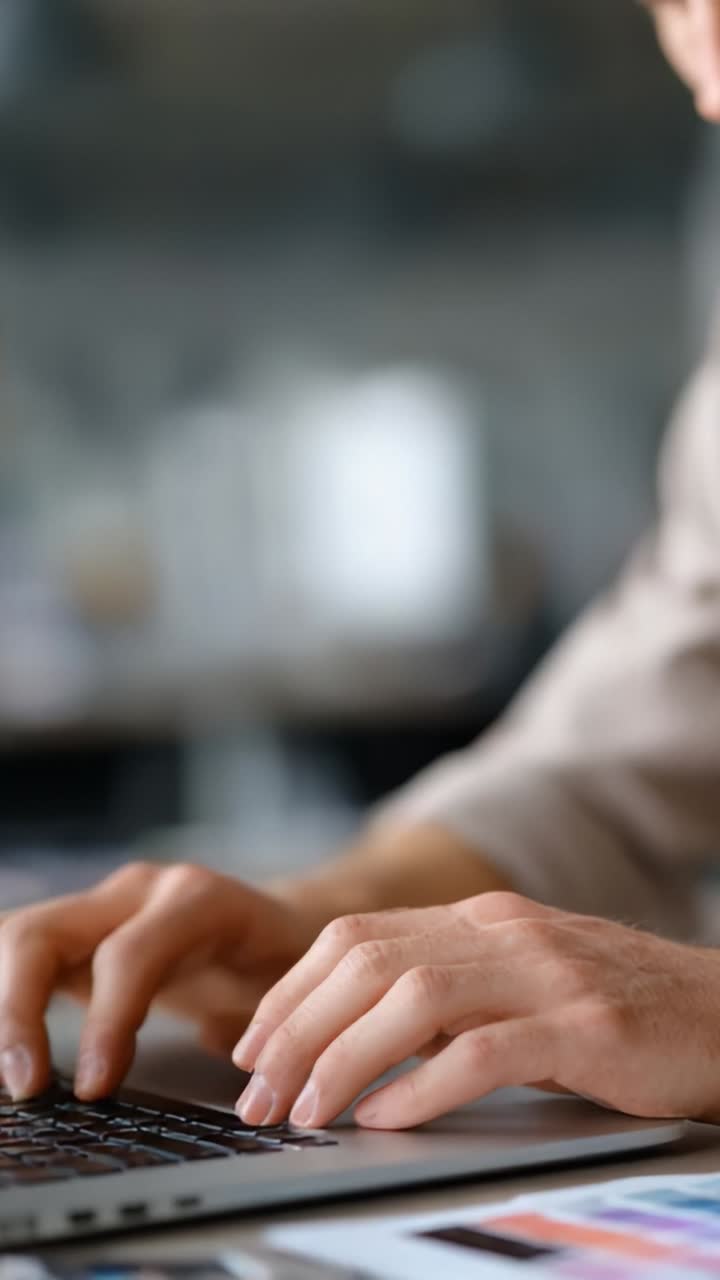 Persona concentrata impegnata in un lavoro produttivo su un portatile, che mostra le mani che digitano su una tastiera in un ambiente ufficio moderno e collaborativo