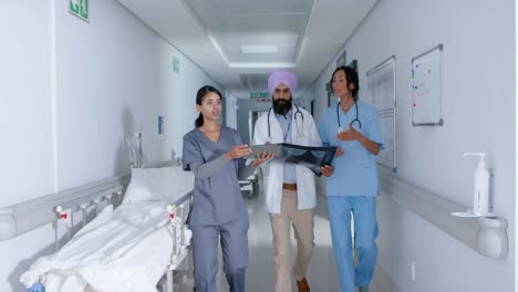Diverse-doctors-and-nurse-using-tablet-and-walking-through-corridor-at-hospital,-in-slow-motion