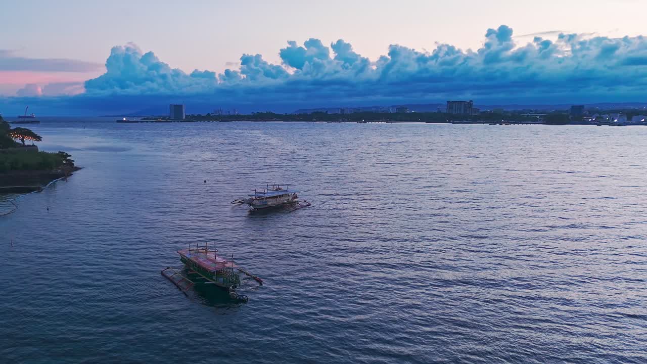 Beautiful 4K drone footage of boats anchored near tropical coastline at twilight. Calm ocean waves and glowing sky create a cinematic travel atmosphere