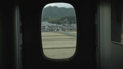 view through a carriage window on a shinkansen or bullet train in japan looking out into the rural countryside