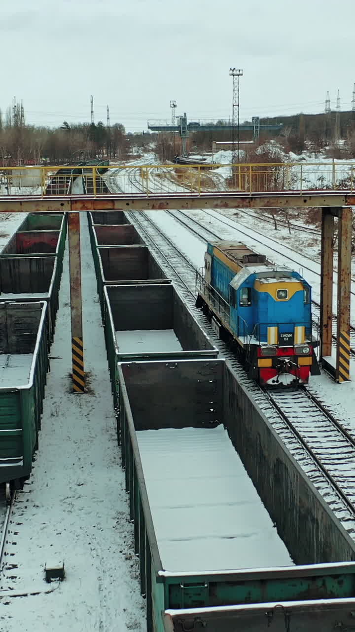 A blue freight train arrives at its destination amid a multitude of containers on a winter day. Aerial view. Vertical video