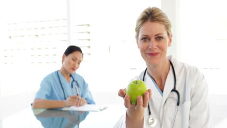 un médico sonriente que muestra una manzana verde