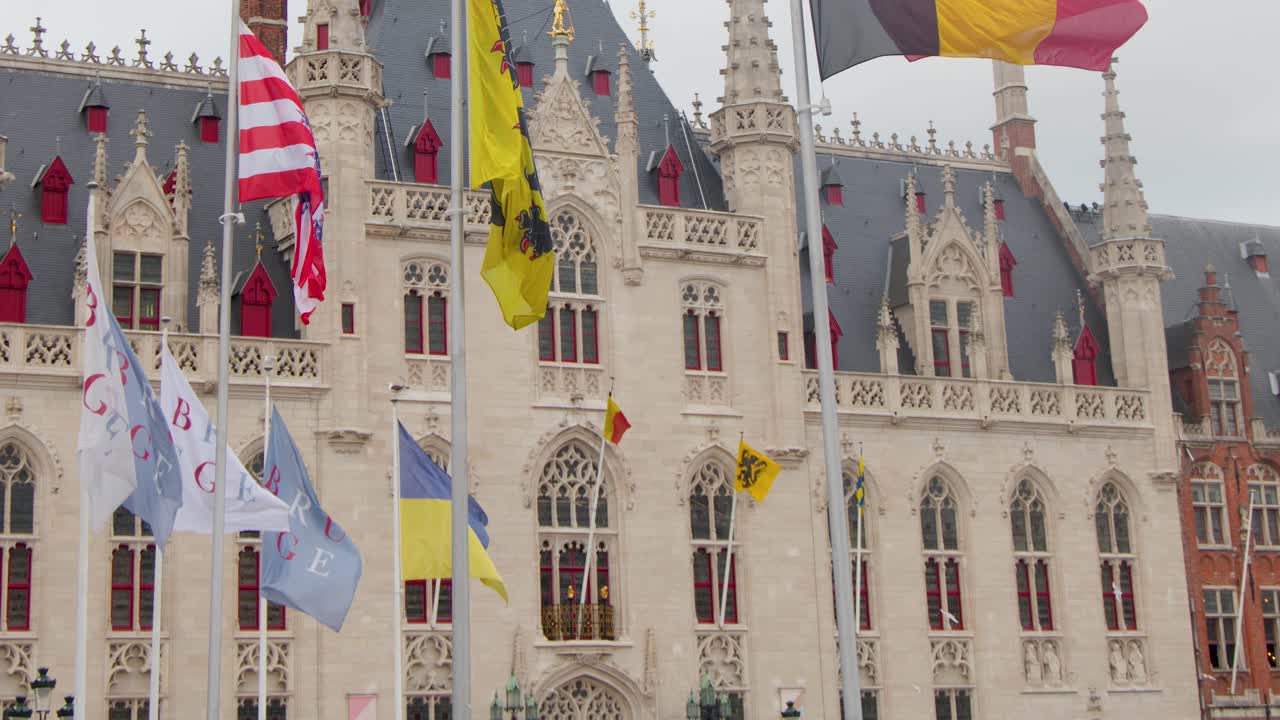 Multiple flags flutter before ornate medieval architecture under overcast daylight, static camera, vibrant atmosphere