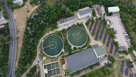 modern water treatment facility featuring two large circular clarifier tanks, solar panel arrays, and surrounding utility buildings. aerial view