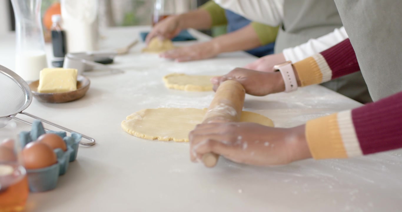 Three women starting from flattened dough, rolling pins smoothing rounds on home counter for baking