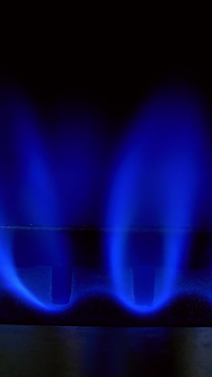 Gas blue flame. Gas stove on black background. Burning natural gas. Switching on fire on stove. Close-up. Vertical video