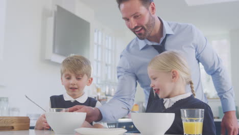 father serves orange juice to children in school uniform eating breakfast as he gets ready for work