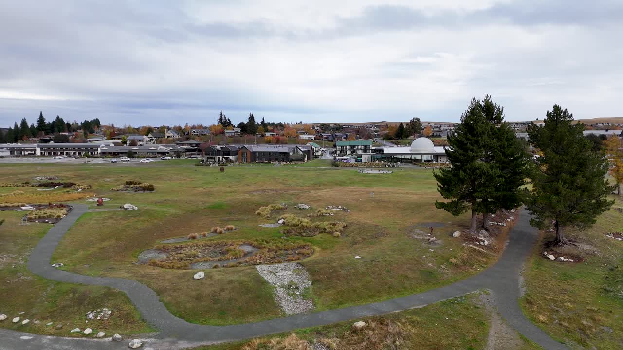 Drone footage captures the serene landscape of Lake Tekapo, highlighting the observatory and surrounding greenery under overcast skies