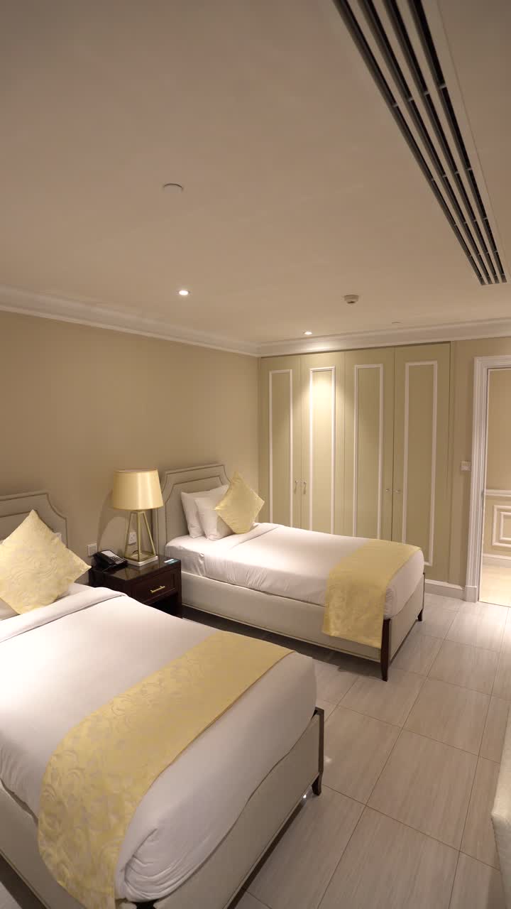 A clean, modern hotel room featuring two single beds with white linens and elegant yellow throw pillows and runners