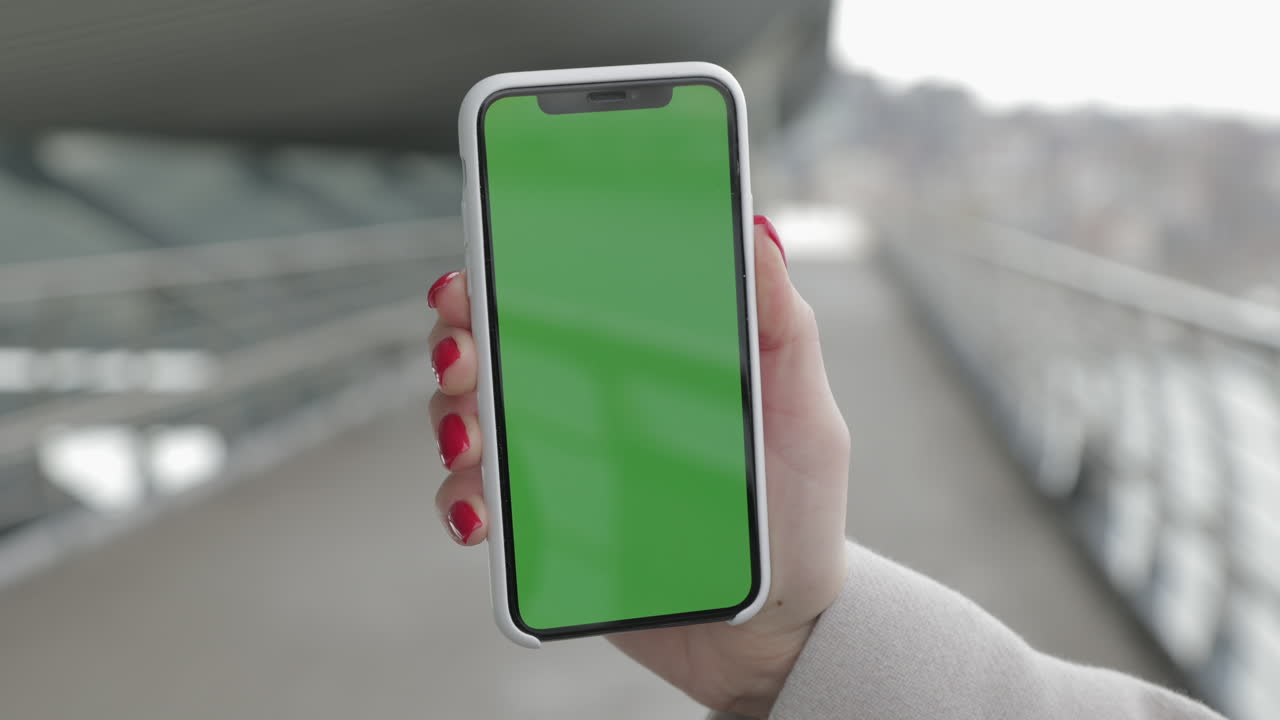Woman holding a smartphone with a green screen outdoors