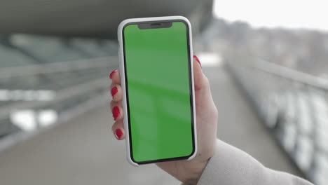 woman holding a smartphone with a green screen outdoors