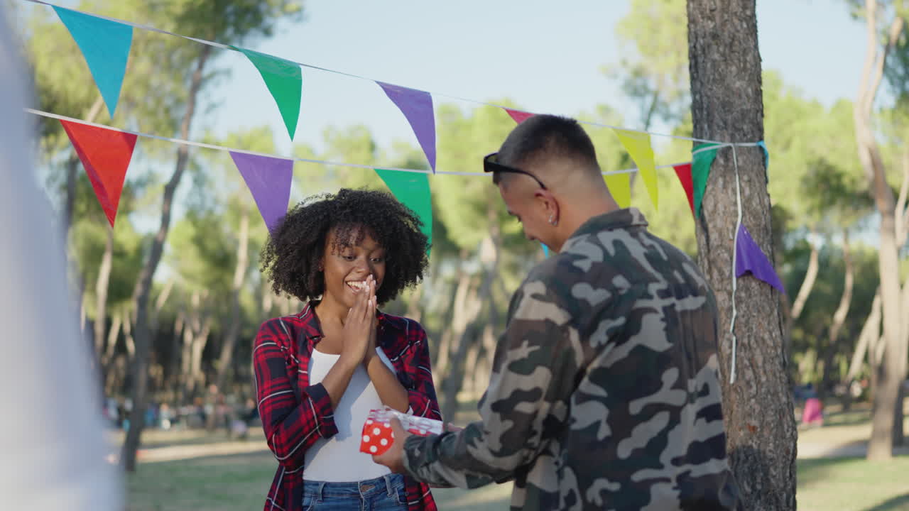 Man surprising a woman with a gift at an outdoor celebration with friends