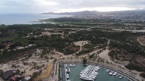 Vista-Aérea-Sobre-Un-Pintoresco-Paisaje-Costero-Con-Vistas-Al-Hermoso-Puerto-Deportivo-De-Puerto-Los-Cabos-Con-Barcos-Estacionados-En-El-Paseo-Marítimo-Durante-Un-Emocionante-Viaje-Por-México