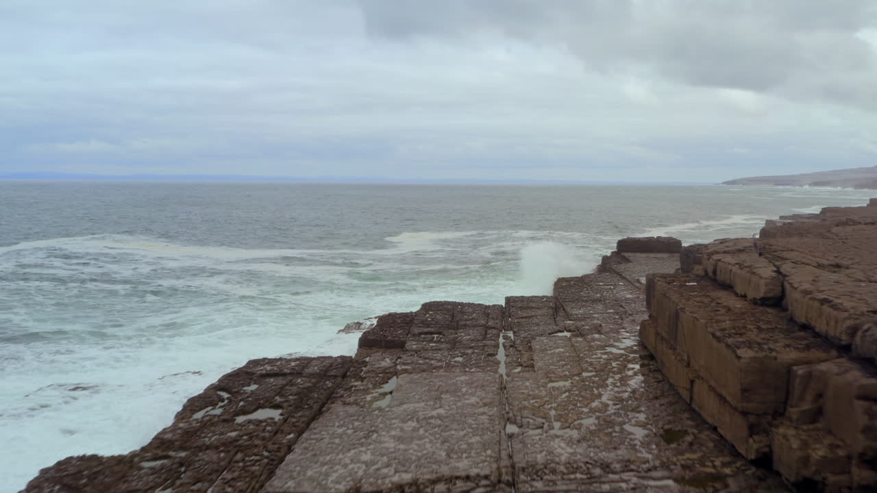 Dynamic tracking shot flies over layered rock formations in Doolin as Atlantic waves crash along the coast