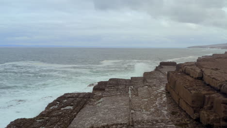 dynamic tracking shot flies over layered rock formations in doolin as atlantic waves crash along the coast