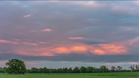 static shot of rainy clouds passing by in timelapse over rural countryside with young green wheat sprouts in summer evening