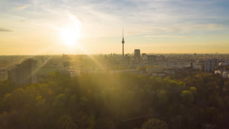 Szenischer-Hyper-Zeitraffer,-Sich-Schnell-Bewegender-Zeitraffer-über-Dem-Stadtbild-Mit-Natur-Und-Skyline,-Berliner-Fernsehturm-In-Goldener-Stunde,-Sonnenuntergangslicht,-Luftaufnahme