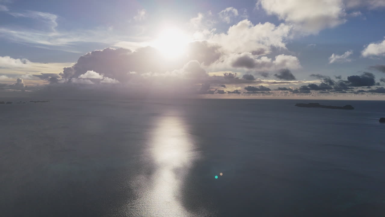 Drone flyover of the vibrant blue ocean and scenic islands of Palau with the sun beginning to set in the horizon. Cinematic aerial drone shot