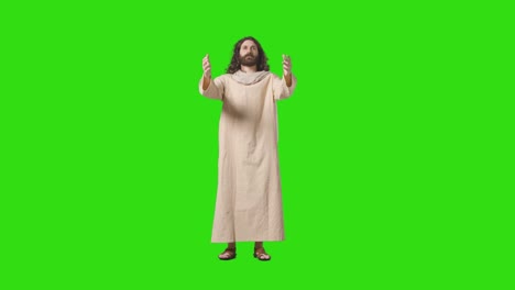 studio shot of man wearing robes and sandals with long hair and beard representing figure of jesus christ raising arms on green screen