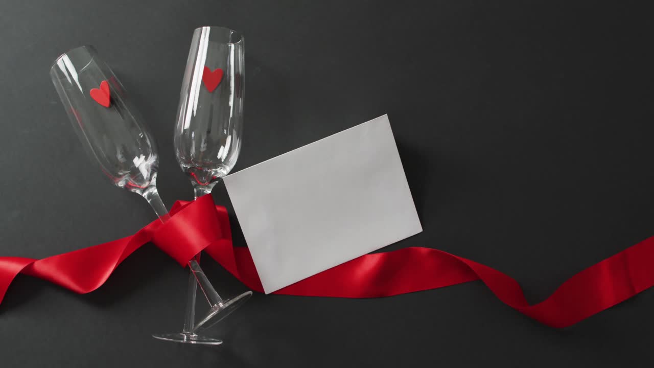 Champagne glasses with hearts, red ribbon and white card with copy space at valentine's day