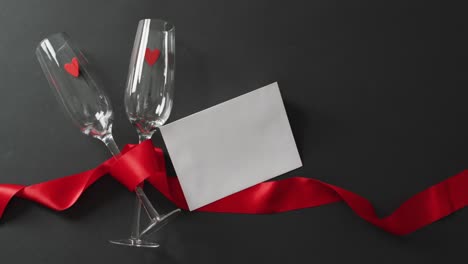 champagne glasses with hearts, red ribbon and white card with copy space at valentine's day