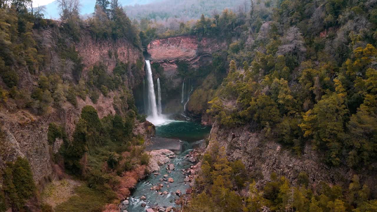 Forward drone aerial of dramatic waterfall cascading into turquoise pool, Siete Tazas National Park, Ñuble, Chile with autumn forest canyon