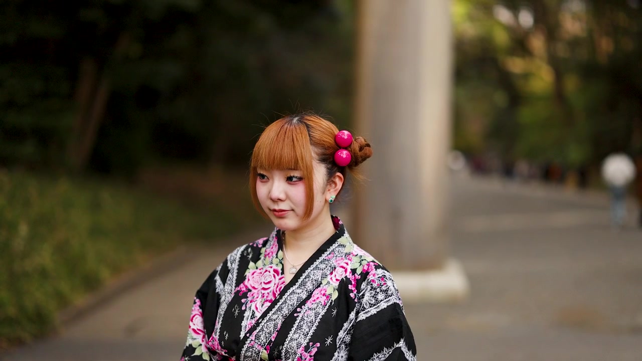 Giovane donna che indossa un kimono floreale si trova in un parco di Tokyo con uno sfondo sfocato morbido.