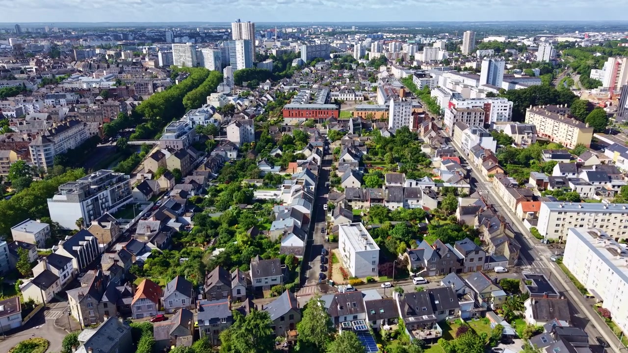 Dron volando hacia adelante sobre un distrito residencial en Rennes con la Tour des Horizons visible al fondo, Francia.