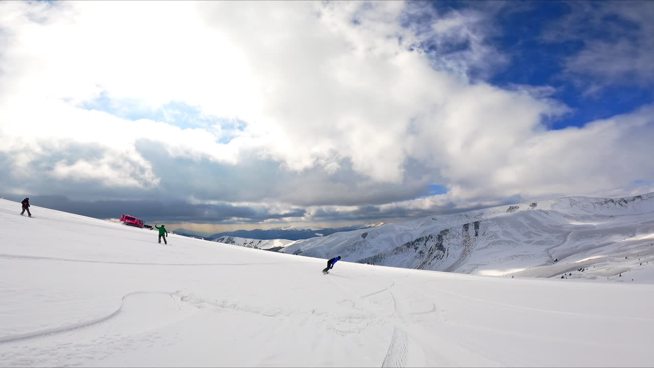 Amazing scenery of the snowy mountains under the white cloudscape. Snowboarders go down the slopes.