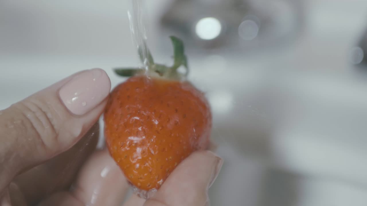 Una fragola viene tenuta e lavata accuratamente sotto l'acqua al rallentatore