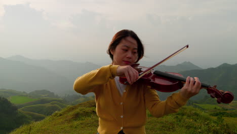 Zoom-Inverso-Perfecto-De-Una-Mujer-Tocando-El-Violín-En-La-Cima-De-Una-Montaña,-Imagen-Increíble