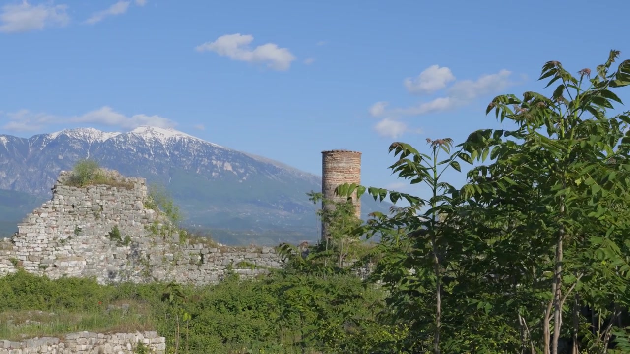 Mura in rovina e torre in mattoni del Castello di Berat di fronte a una catena montuosa innevata in Albania
