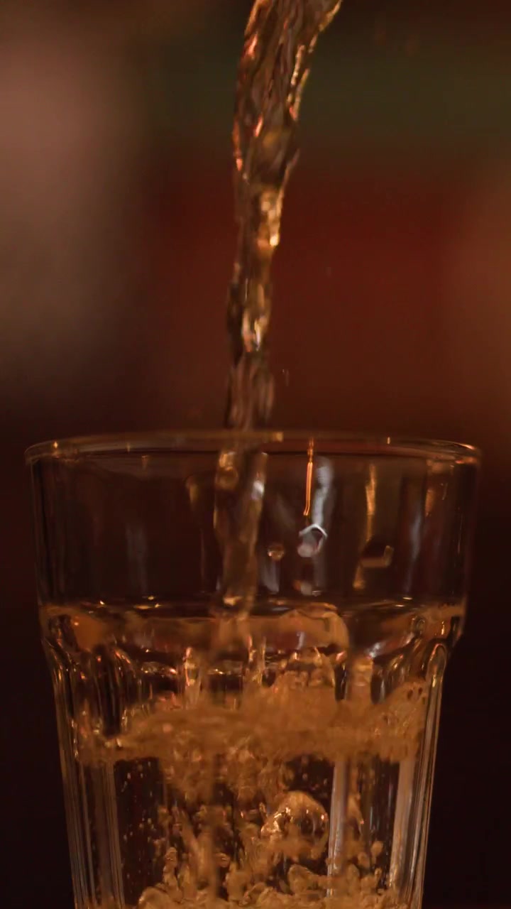 Acqua frizzante trasparente si versa in un bicchiere a coste con bollicine ed effervescenza in una luce calda.