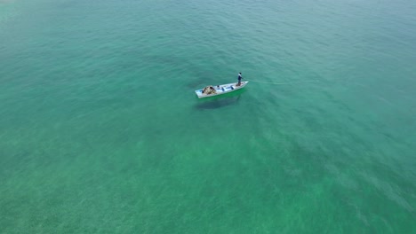 Spectacular-aerial-view-of-a-fisherman-in-his-boat-on-Tobago's-white-sand-beach-and-clear-blue-waters-in-the-Caribbean