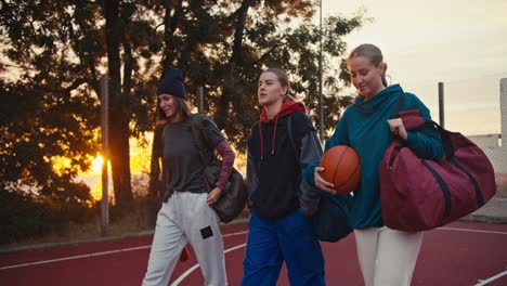 a happy company of girls basketball players walk along the basketball field with a ball in their hands and communicate early in the morning at sunrise