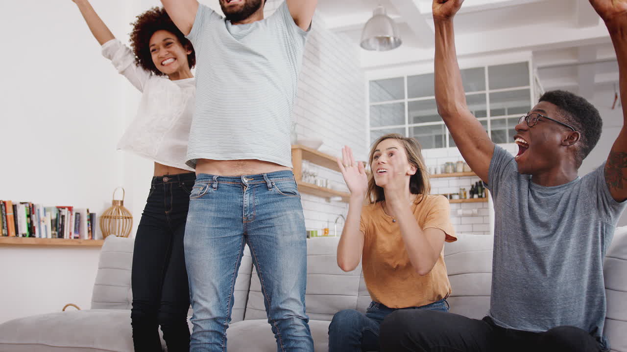 Excited Group Of Friends Sitting On Sofa Watching Sports On TV And Celebrating