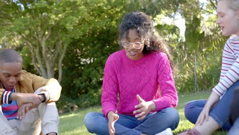 Happy-diverse-group-of-teenage-friends-sitting-on-grass-and-talking-in-sunny-park,-slow-motion